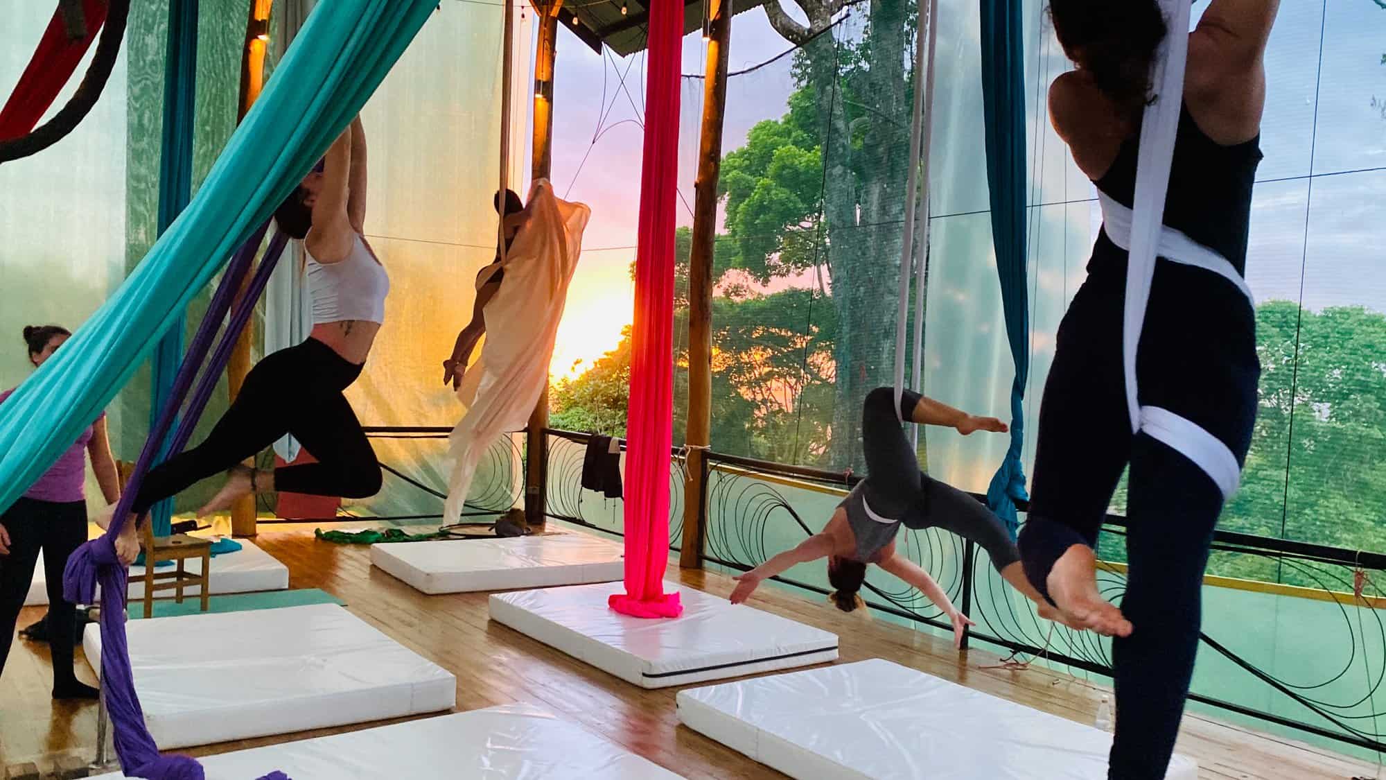 Aerialists training on silks at sunset on the open-air deck at Airborne Arts, with the Costa Rican mountains in the background